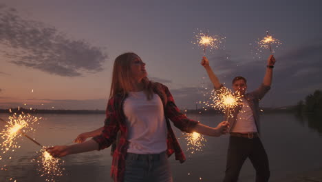 Tanzende-Freunde-Mit-Feuerwerk-Haben-Spaß-Und-Feiern-Gemeinsam-Den-Feiertag,-Jungs-Und-Mädels-Im-Sommer-Am-Strand.-Wunderkerzen-In-Den-Händen-Von-Leuten,-Die-Spaß-Haben.