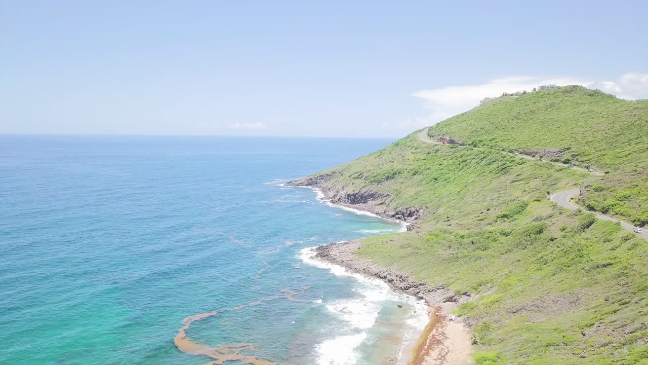 Aerial view of the shore of St Kitts with rough waters hitting it and cars driving on the road.