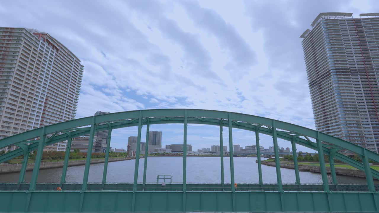 A shot of the old Harumi Railway Bridge, with its green metal arch, connecting the city's modern buildings
