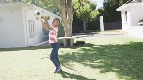 african american boy playing football in garden, in slow motion