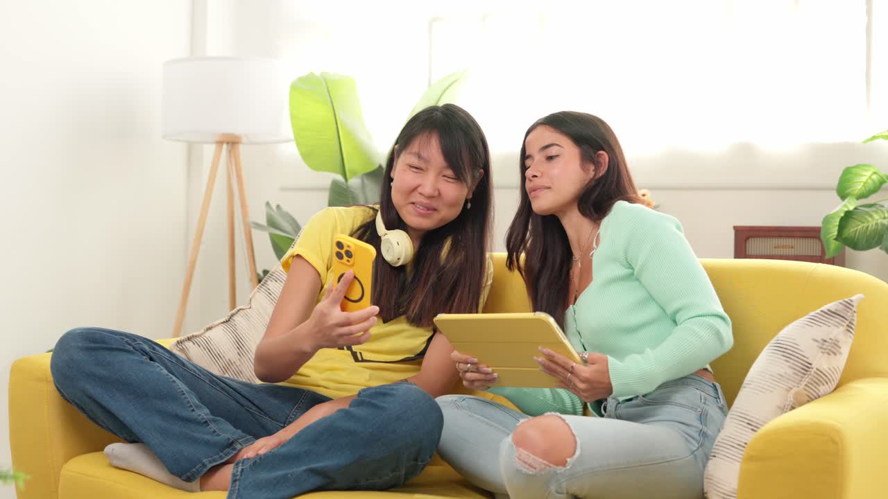 Two friends using a tablet and a cell phone on a couch