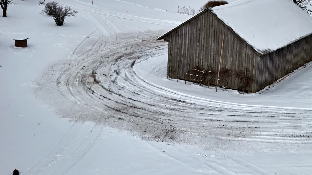 Aerial view of a vehicle drifting on a snowy road around a barn