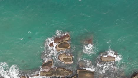 Vista-Aérea-De-Las-Olas-Del-Océano-Rompiendo-En-La-Bahía-Rocosa