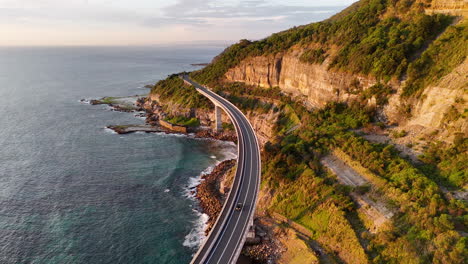 filmische tracking-dron-aufnahmen eines fahrzeugs entlang der ikonischen sea cliff bridge, die atemberaubende küstenlandschaften zeigen.