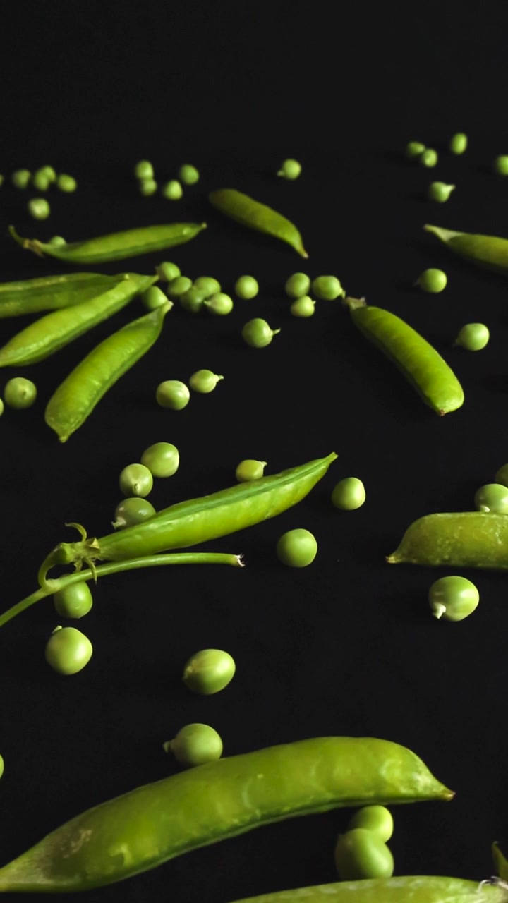 Smooth gliding camera movement over fresh green pea pods and scattered peas on a dark background. This detailed macro view highlights the organic texture and vibrant color of the healthy vegetable