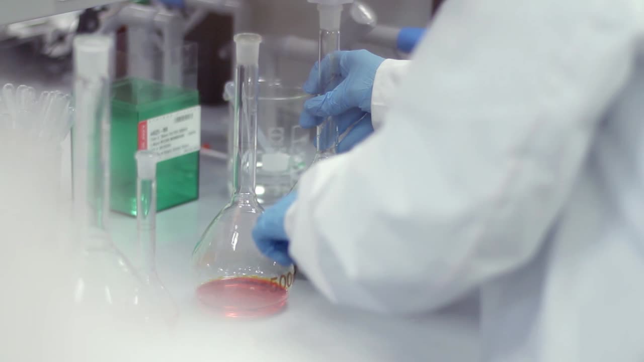 Scientist in Lab Coat Handling Volumetric Flask with Green Liquid
