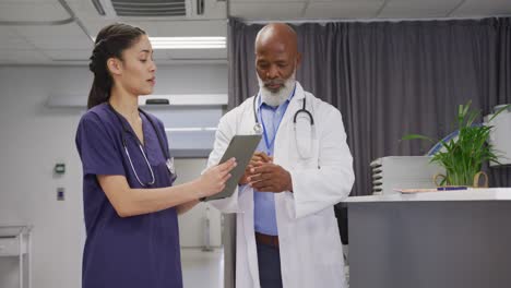 Diverse-male-and-female-doctors-using-tablet-and-talking-at-hospital