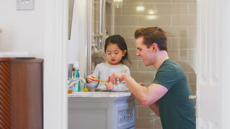familia con el padre ayudando a la hija con la pasta de dientes mientras se cepilla los dientes en el baño