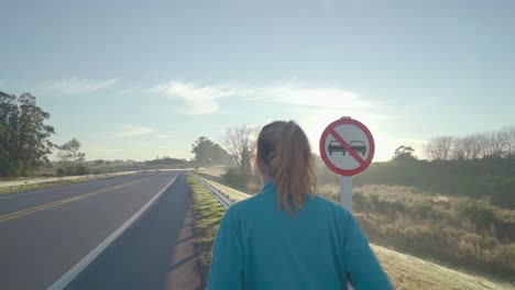young woman runs down the road in the morning. the sun is just beginning to rise on the horizon and flares reflect on the camera lens.