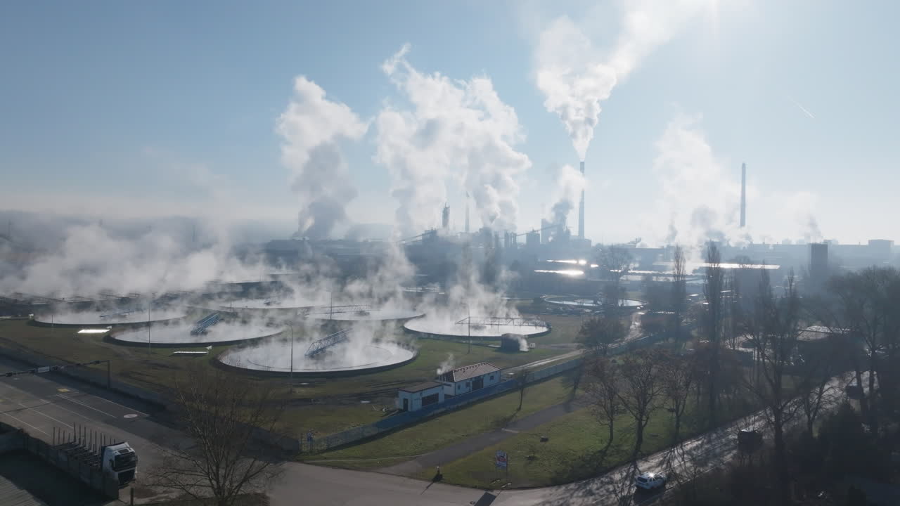 Ripresa con drone a bassa quota del complesso della cartiera di Štětí con numerose ciminiere che rilasciano vapore, bacini industriali, strade vicine e alberi invernali alla chiara luce del mattino