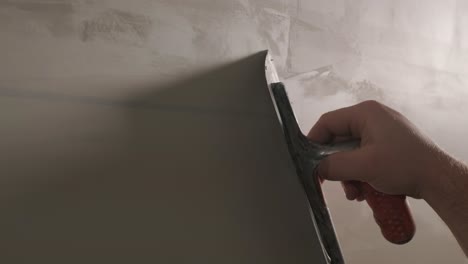 man plastering the walls with finishing putty in room with putty spatula