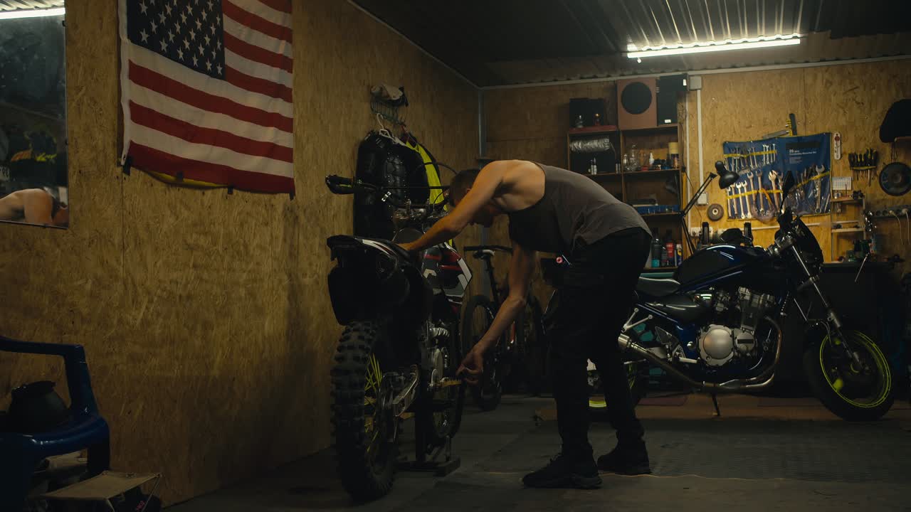 짧은 헤어과 회색 크 을 입은 남성 메카닉은 오토바이 부품을 수리하고 작업하는 동안 도구와 함께 그의 차고 작업장에서 자이크에 자전거를 니다.