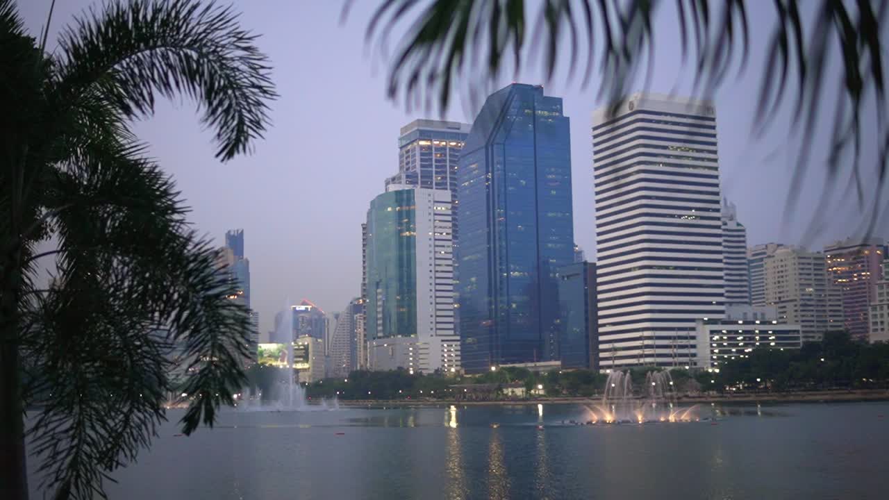 Grattacieli di fronte al lago dal Parco Benjakitti nella città di Bangkok, Thailandia, carrellata dinamica in avvicinamento
