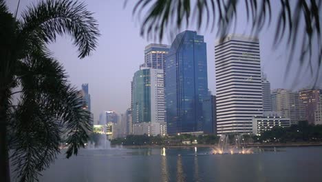 Tall-buildings-across-the-lake-from-Benjakitti-Park-in-the-city-of-Bangkok,-Thailand-dynamic-dolly-in