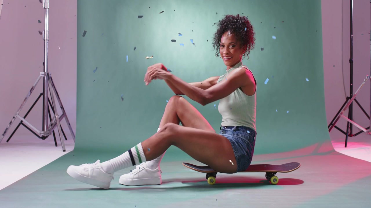 Confetti falling leading model shifting on skateboard, adjusting pose, smiling during fashion shoot