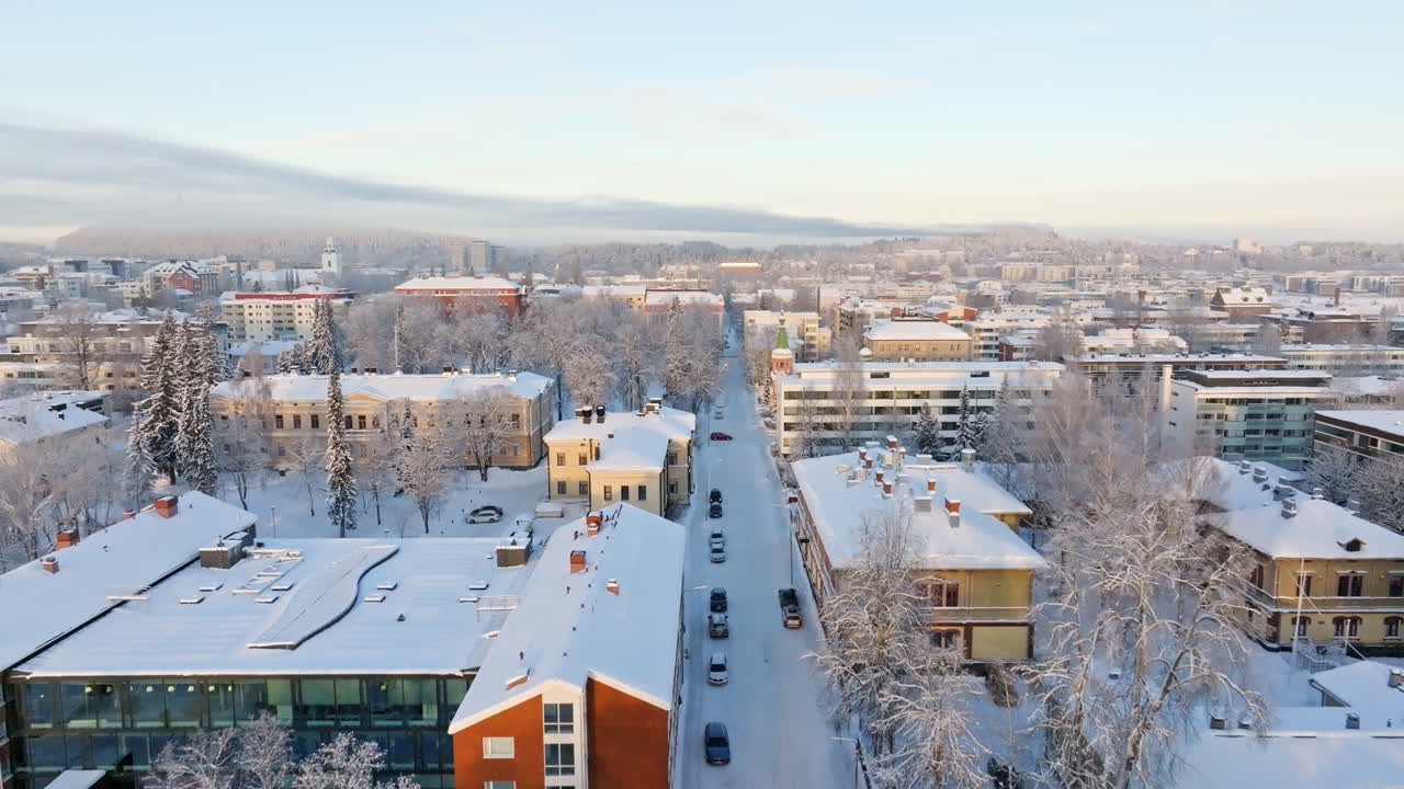 Aerial view backwards over snowy streets in Kuopio city, winter sunrise in Finland