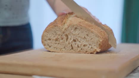 Cutting-fresh-loaf-of-bread-with-a-knife,-side-view