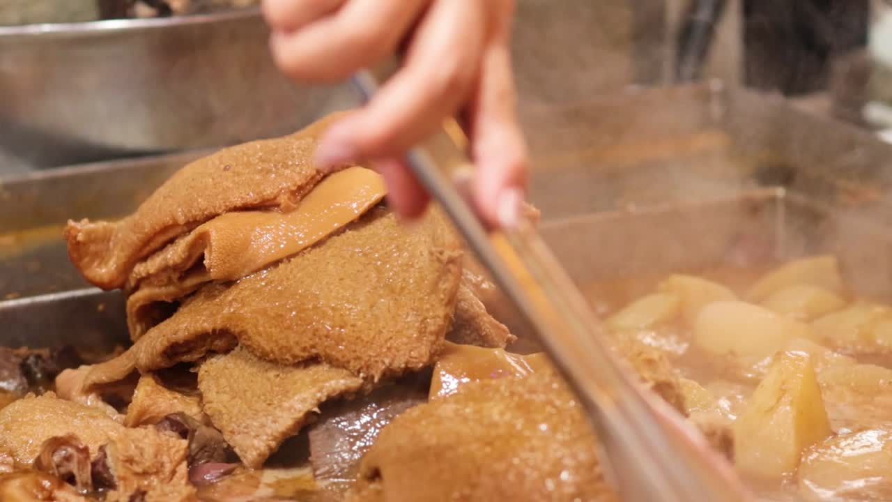 Close-up of hands using tongs to prepare offal in a steaming broth.