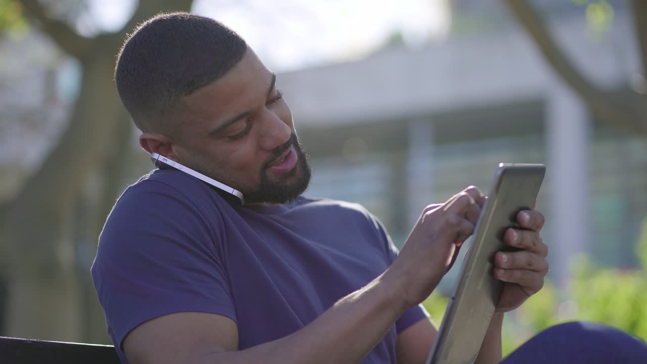 Man in park talking on phone, searching information on tablet