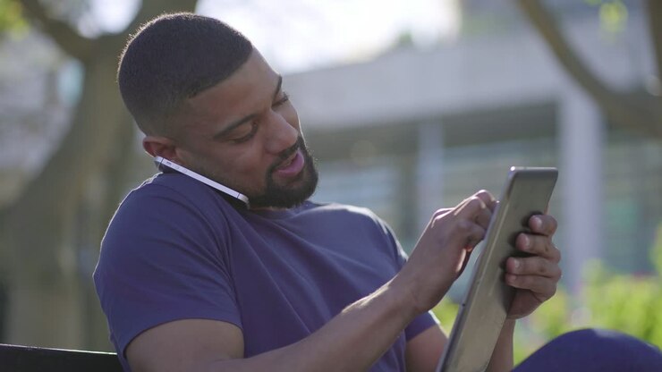 Man in park talking on phone, searching information on tablet