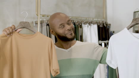 bearded black guy choosing between two t-shirts in clothing shop