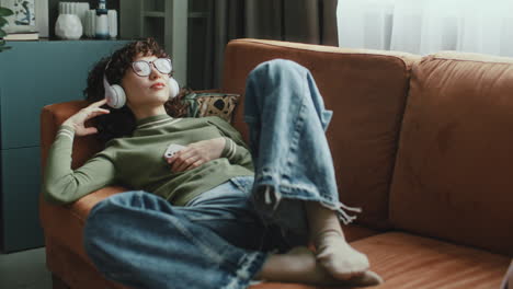 girl in headphones relaxing on couch, listening to music with eyes closed