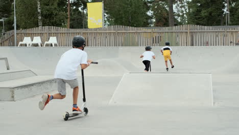 three friends boys riding ride kick bike kickbikes scooter electric scooters skateboard skate park concrete ramp jump jumps of edge flying tricks kid stunt professional summer camp cool evening boy