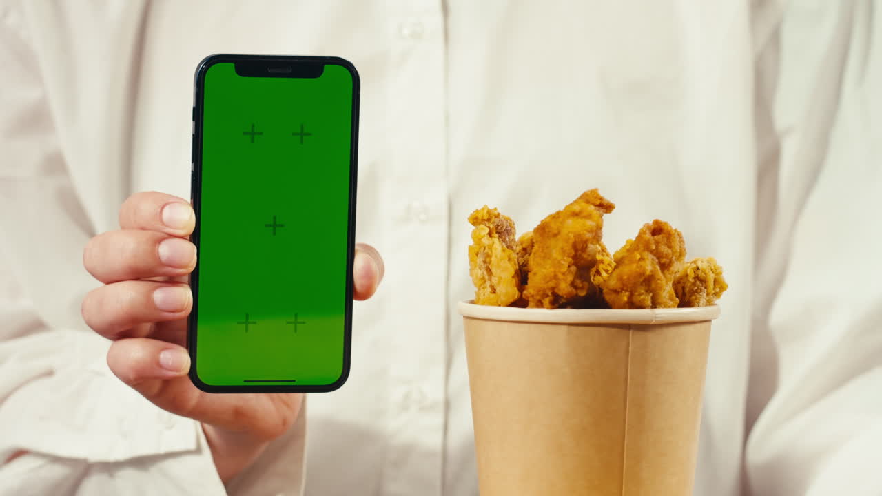 Person holding a phone with a green screen and a container of fried chicken