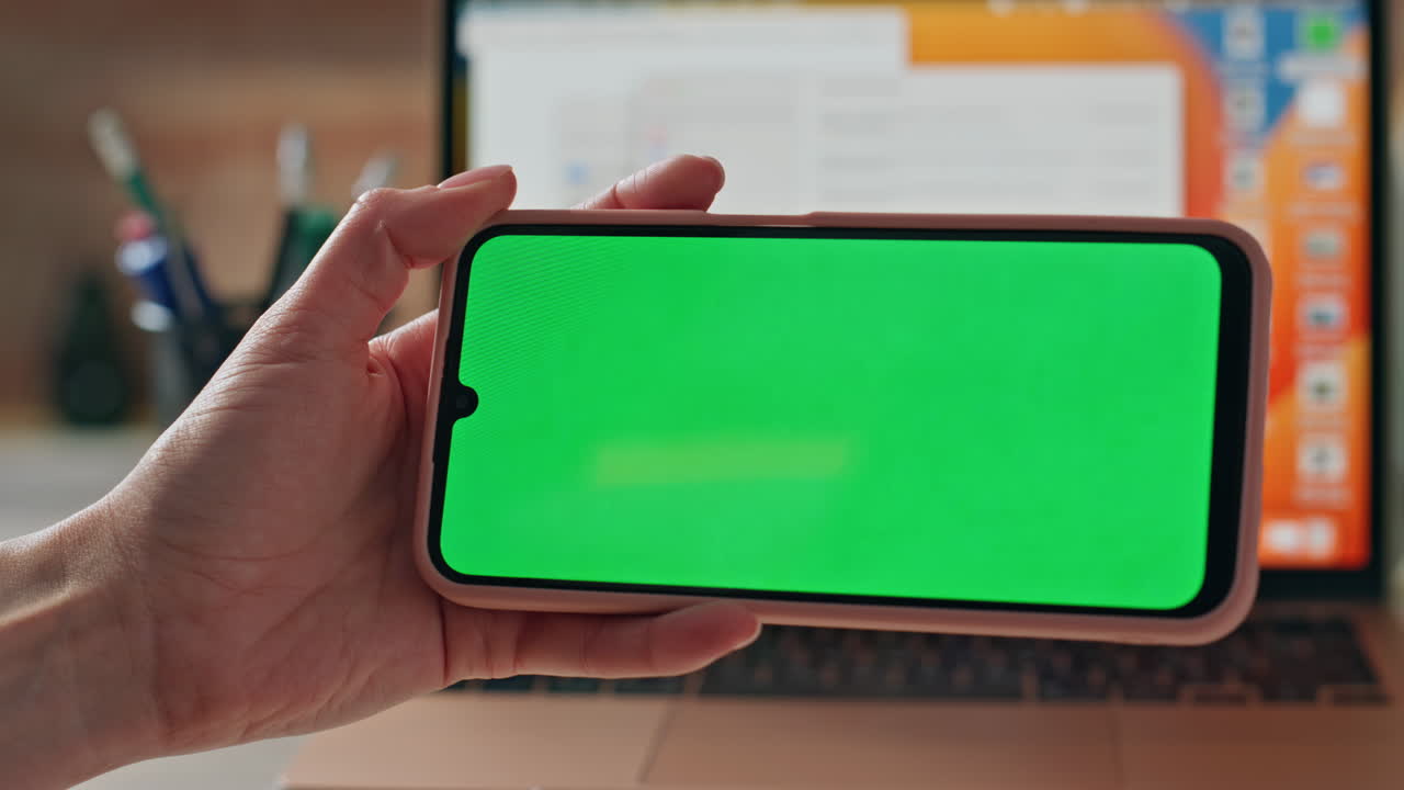 Girl watching video mockup mobile phone at work desk with laptop close up.