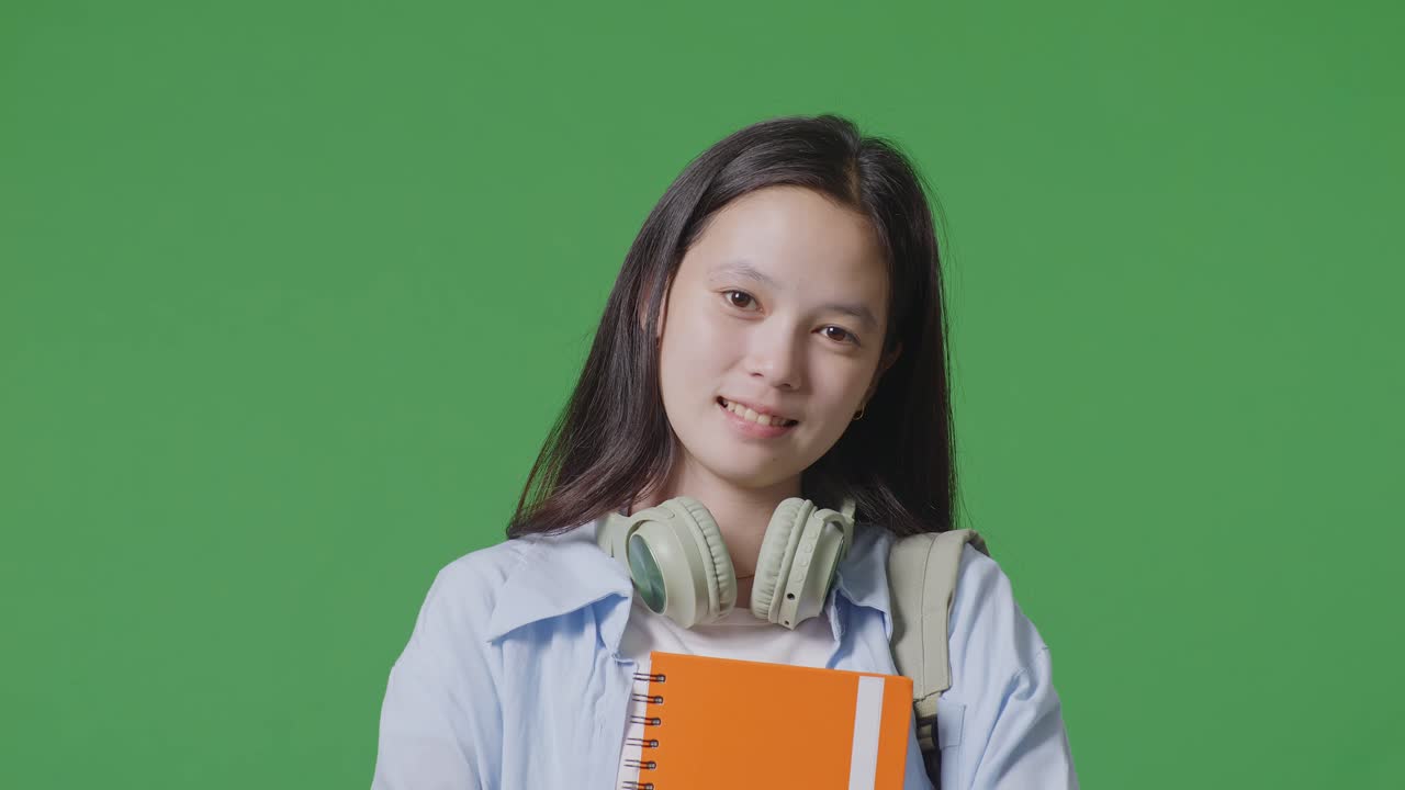 緑の画面の背景のスタジオに立っている間バックパックを持ったアジアのティーンエイジャーの女の子の学生のクローズアップ