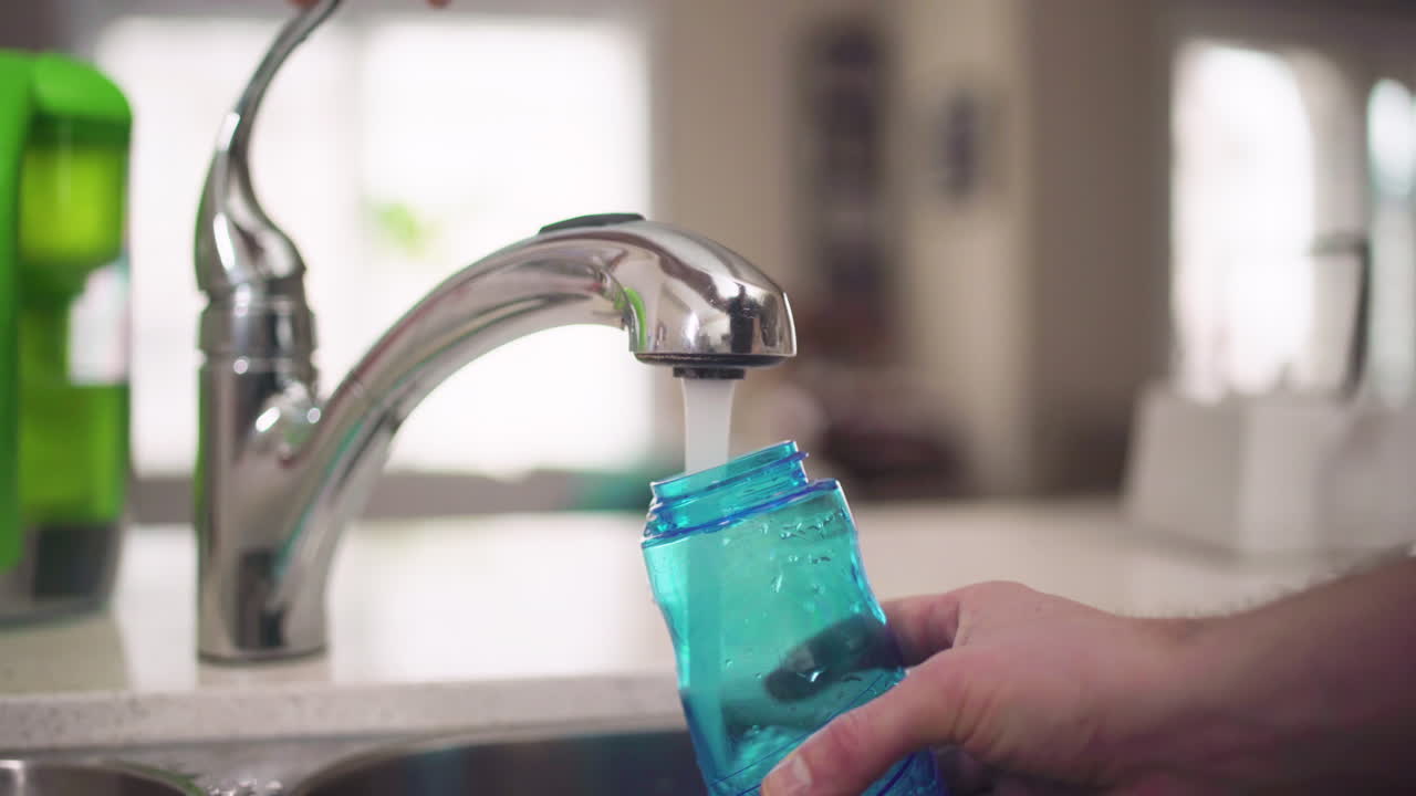 mano llenando una botella de agua de un grifo de cocina