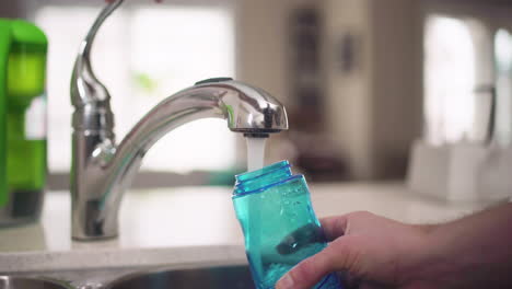 hand filling up a water bottle from a kitchen tap