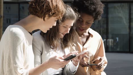 three women with smartphones standing on street