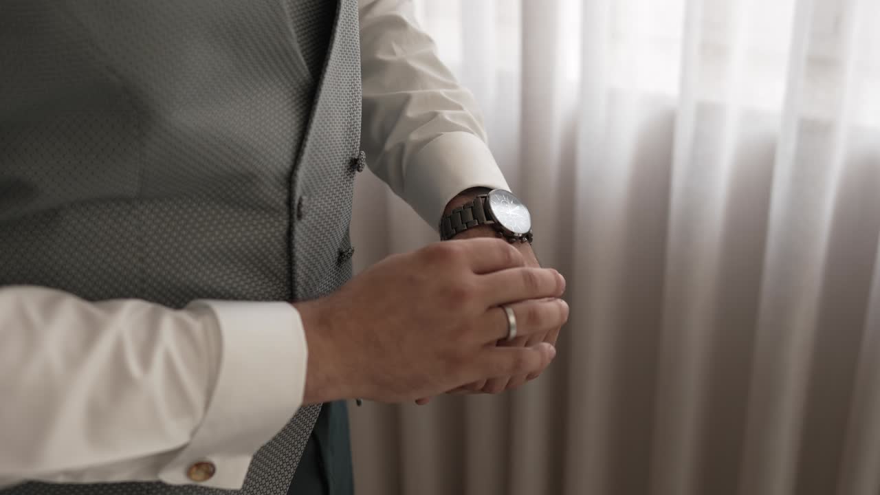 close up of groom adjusting wristwatch in daylight near white curtains