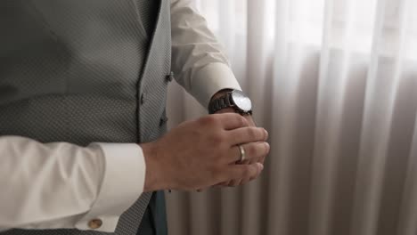 close up of groom adjusting wristwatch in daylight near white curtains