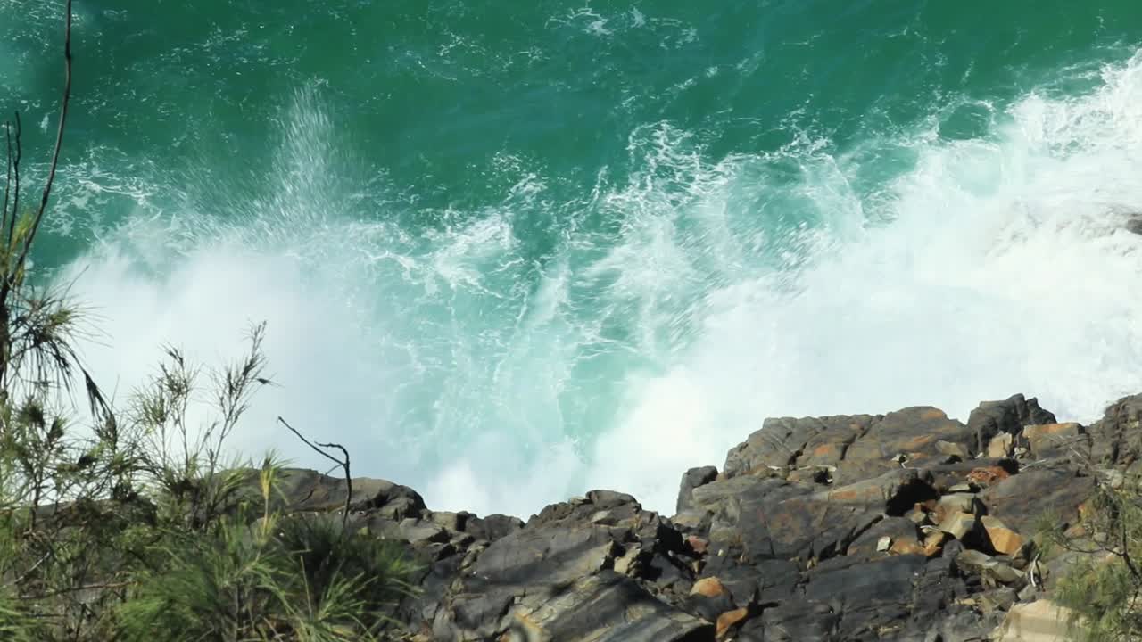Waves crash into rocky coast sending sea spray into the air.