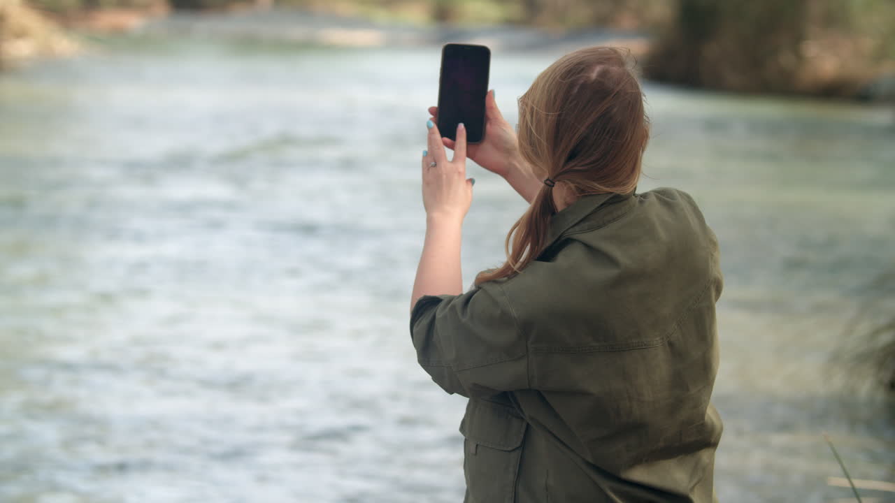 mujer con teléfono inteligente tomando fotos del río