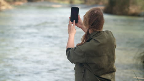 woman with smartphone taking pictures of the river