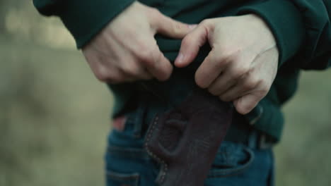 una vista de cerca de un hombre cargando una pistola, la escena se centra en las manos, la funda y parte de los vaqueros mientras se aleja, con un borrón que rodea