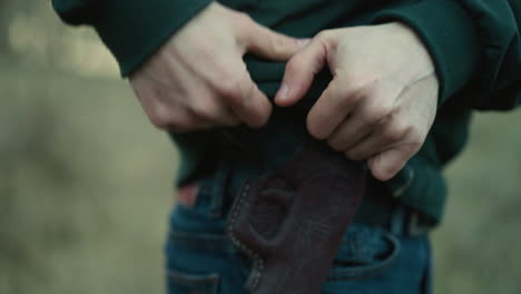 a close view of a man holstering a handgun, the scene focuses on the hands, holster, and part of the jeans as he walks away, with a blur surrounding