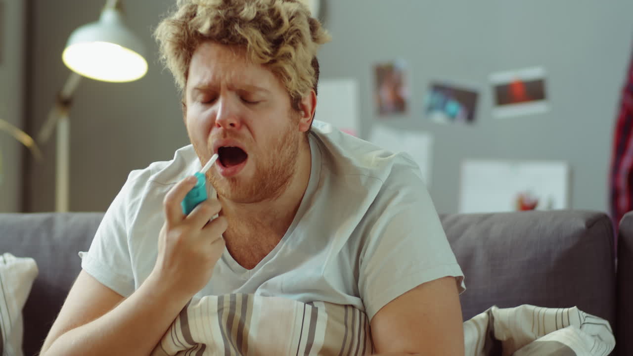 hombre enfermo tosiendo y usando spray para la garganta en casa