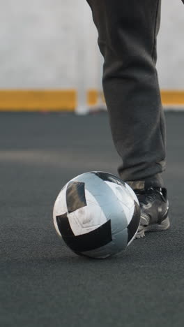 vista de la pierna de un hombre realizando giros precisos del tobillo con las piernas izquierda y derecha, equilibrando una pelota de fútbol en una arena deportiva con poste de portería y pared pintada