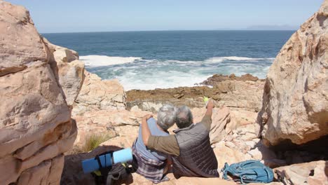 Happy-senior-biracial-couple-in-mountains-embracing-at-sea,-in-slow-motion