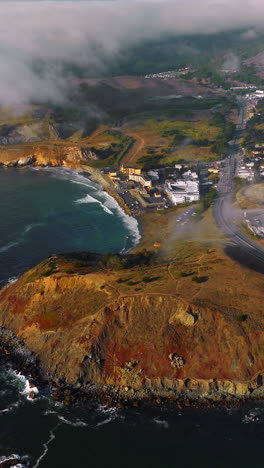 sunny rocky coastline with houses and highway on top. thick fog crawling to the city. aerial perspective. vertical video