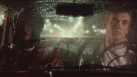 young couple sitting inside retro car during rainy night drive