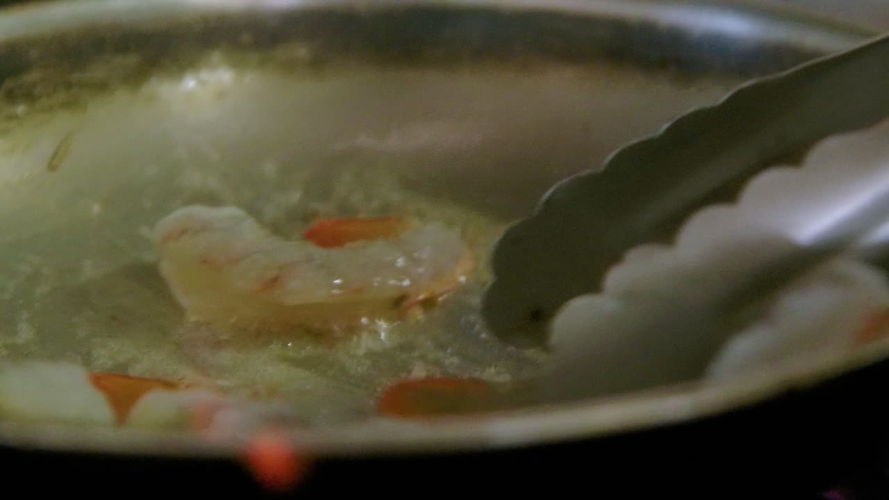 el chef frita camarones en una sartén llena de ajo y mantequilla burbujeando, una pequeña llama estalla