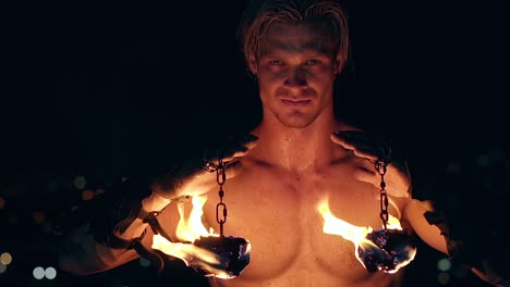 young blond male holds two burning pois hanging on chains slow motion close-up