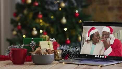 Pareja-De-Ancianos-Afroamericanos-Con-Sombreros-De-Santa-En-Videollamada-En-Una-Computadora-Portátil,-Con-árbol-De-Navidad