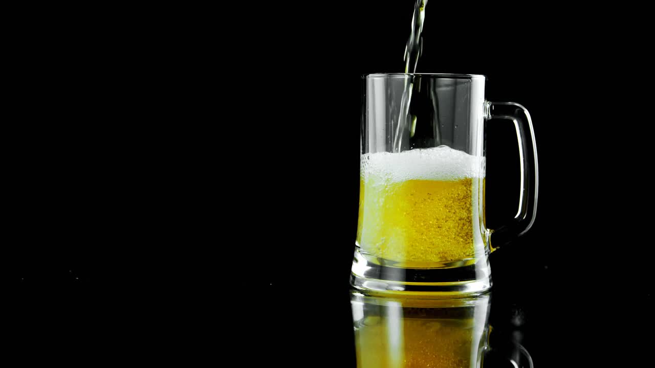 cerveza vertida en una taza de cerveza contra un fondo negro 4k