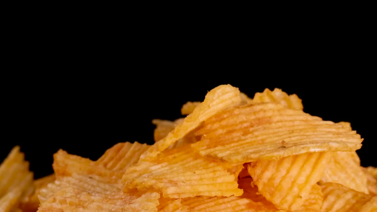 Close-up of a hand reaching into a pile of golden ridged chips against black